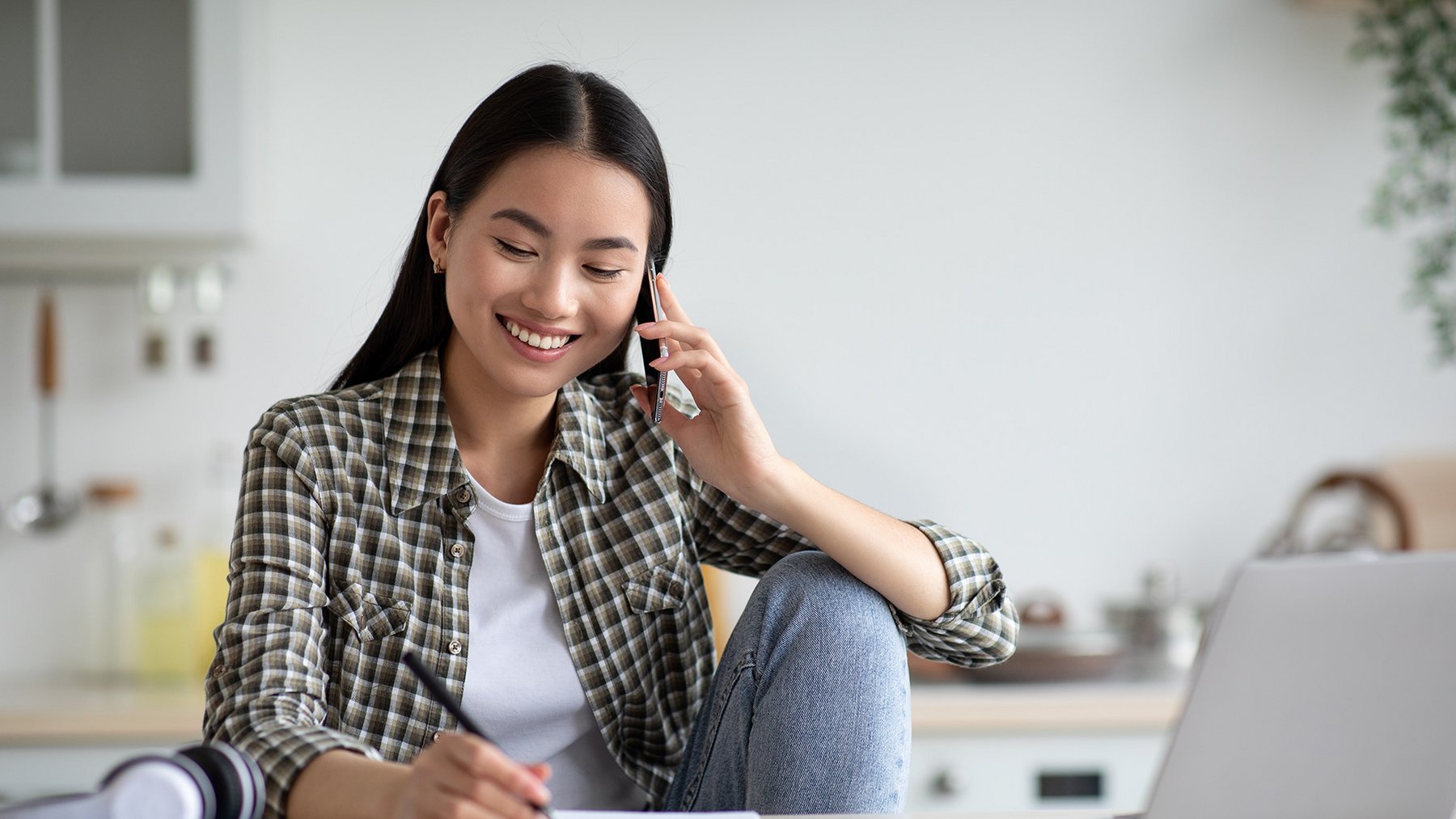 Frau telefonierend am Tisch mit Laptop